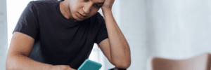 Young man sitting with his head resting on his hand while looking at his phone.